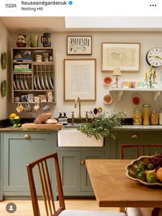 a kitchen with green cabinets and pictures on the wall above the sink, next to a wooden dining table