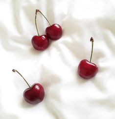 three cherries sitting on top of a white sheet