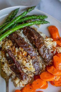 a plate with meat, rice and carrots on it next to asparagus