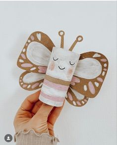 a hand holding up a paper butterfly with eyes closed and pink stripes on it's wings