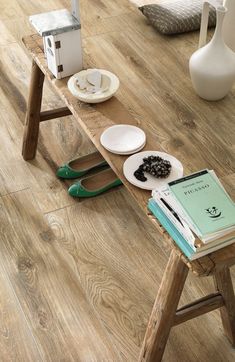 a wooden table topped with books and plates next to a vase on top of a hard wood floor