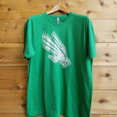 From the heartland to the coasts, wear your Mean Green on your sleeve with your new favorite North Texas t-shirt from us at Nudge Printing! Every shirt is printed by hand with eco-friendly inks on ethically and sustainably sourced garments and then inspected and packaged individually so you know you're getting the best every time. Our shirts are 60% cotton, 40% polyester, so it feels better, breathes easier, and will last longer than your average 100% cotton t-shirt. It is also preshrunk to supp Diving Eagle, Michigan Hoodie, Loyola University Chicago, University Of North Texas, Chicago University, Mean Green, Eagle Logo, North Texas, Baseball Shirts