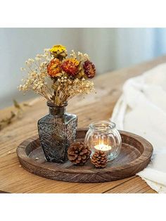 two vases with flowers are sitting on a wooden tray next to a lit candle