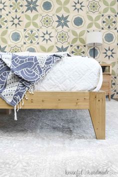 a bed with a blanket on it in front of a wallpapered wall and floor