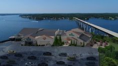 an aerial view of a restaurant and parking lot near the water with a bridge in the background