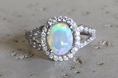 "A lovely Halo Setting featuring an oval-shape genuine top-notch Welo Opal with a magnificent play of color, complemented with a split shank embellished with pave set cubic zirconia handcrafted in Sterling Silver. Wrapped in a box ready for gift-giving.(r-egt-70 ) FINAL SALE Ring Info ----------------- *Opal measure 6mm x 8mm *Opal with Halo measure 11.5mm x 10mm *Ring Shank Width 2mm *Stone height 8mm *Model ring size 5 HOW TO CARE FOR YOUR OPAL --------------------------------------------- Opa Moissanite Opal Engagement Ring, Oval Opal Ring With Accent Stones, Oval Opal Ring With Gemstone Accents For Anniversary, Oval Opal Ring With Halo Setting, Dazzling Oval Opal Ring For Anniversary, Dazzling Oval Opal Ring, Oval Promise Ring, Juelz Santana, Opal Promise Ring