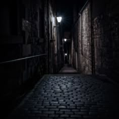 a dark alley with brick pavement and street lights