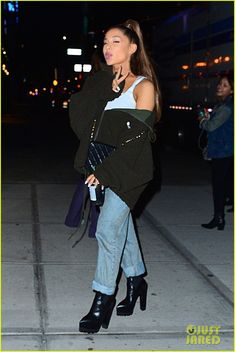 a woman is walking down the street at night with her hand in her pocket and wearing high heeled boots