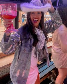 a woman holding up a wine glass in front of her face and wearing a hat