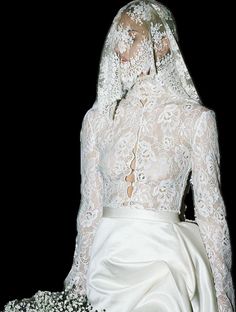 a woman in a white wedding dress and veil with flowers on her head sitting down