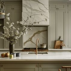 a kitchen with marble counter tops and white cupboards, an island style sink and a large metal faucet