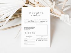 a white wedding program sitting on top of a table next to some palm leaves and flowers