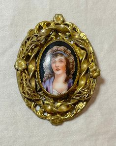 This antique brooch is a stunning piece of jewelry that will surely catch anyone's attention. Made of ornate gold gilded brass and adorned with an intricate hand-painted porcelain medallion, this brooch is a true masterpiece. It features a painted portrait of a lovely middle aged lady and signed underneath.. The brooch is perfect for collectors of antique jewelry and those who appreciate the beauty of unique pieces. Its intricate design and attention to detail make it a true conversation starter Gold Art Nouveau Brooch For Collectors, Ornate Medallion Brooches For Collectors, Ornate Medallion Brooches For Collectibles, Antique Bronze Brooches For Collectors, Antique Bronze Collectible Brooches, Ornate Antique Gold Brooches For Collectors, Ornate Gold Collectible Brooches, Victorian Enamel Collectible Pin, Victorian Enamel Pin Collectible