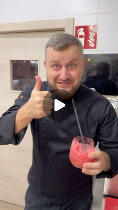 a man with a beard holding a drink and giving the thumbs up sign in front of him