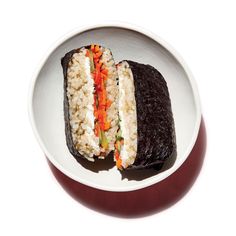 a white plate topped with a cut in half sandwich next to rice and carrots