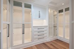 an empty walk in closet with white cabinets and drawers on the wall, along with wood flooring