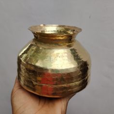 a hand is holding a gold colored vase