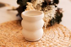 a white vase sitting on top of a woven place mat next to other plants and flowers