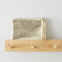 a gold pouch sitting on top of a wooden shelf next to two pegs and a white wall