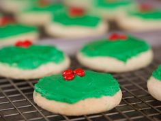 cookies decorated with green icing and red berries are cooling on a rack in the kitchen