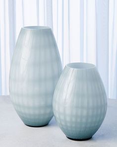 two vases sitting on top of a table next to each other in front of curtains