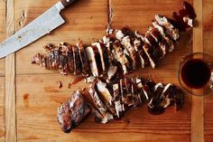 sliced meat on a cutting board next to a knife and glass of wine with sauce