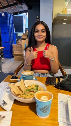 a woman sitting at a table in front of a bowl of food and two cups of coffee