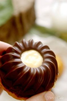 a hand holding a chocolate covered doughnut with cream filling in it's center