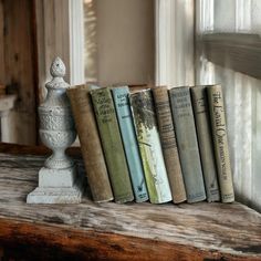 a row of old books sitting on top of a wooden shelf next to a window