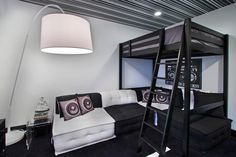 a loft bed with black and white furniture in a room that is well lit by a floor lamp