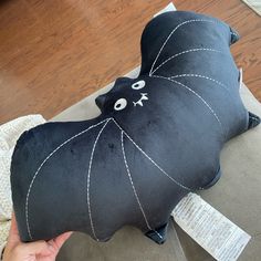 a black bat shaped pillow sitting on top of a couch next to a person's hand