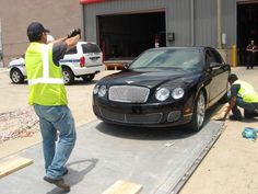 two men in yellow vests standing next to a black car and another man with a camera