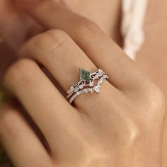 a woman's hand holding a ring with an emerald and white diamond in it