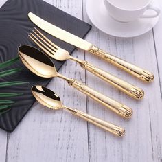 four gold colored forks and spoons on a black place mat next to a cup