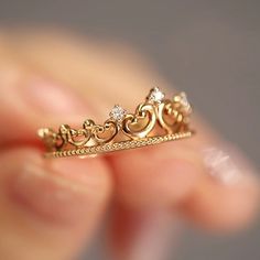 a close up of a person's hand holding a gold ring with hearts on it