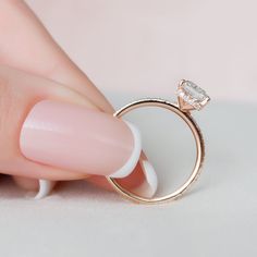 a woman's hand holding a ring with a diamond on it and the tip of her finger