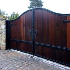 a large wooden gate with black iron bars on the top and bottom, in front of a brick wall