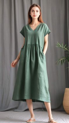 a woman standing in front of a gray curtain wearing a green dress with short sleeves