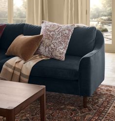 a blue couch with several pillows on it in front of a large window and rug