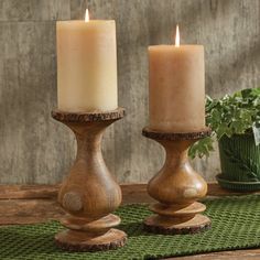 two candles sitting on top of a wooden table next to a potted green plant