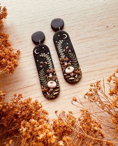 two black and white earrings sitting on top of a wooden table next to dried flowers