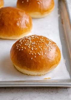 three buns with sesame seeds sit on a baking sheet