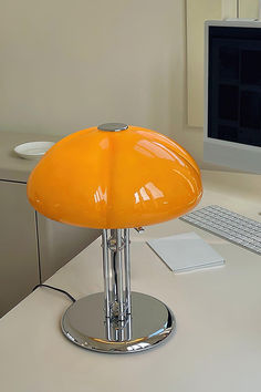 an orange table lamp sitting on top of a desk next to a computer monitor and keyboard