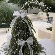 a christmas tree is decorated with white bows and greenery for the holiday season in an outdoor setting