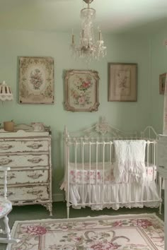 a white crib in a green room with pictures on the wall and chandelier