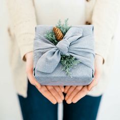 a person holding a wrapped present with a pine cone on it's top and tied in a bow