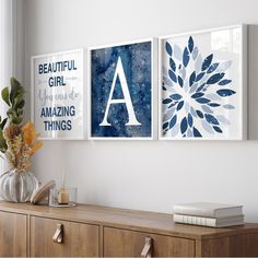 three blue and white art pieces hanging on the wall above a wooden dresser in a living room