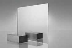 a square mirror sitting on top of a white floor next to a black and silver object