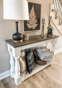 an entryway with a bench, lamp and pillows on the floor next to it