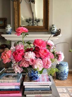 a vase filled with pink flowers sitting on top of a table next to a pile of books